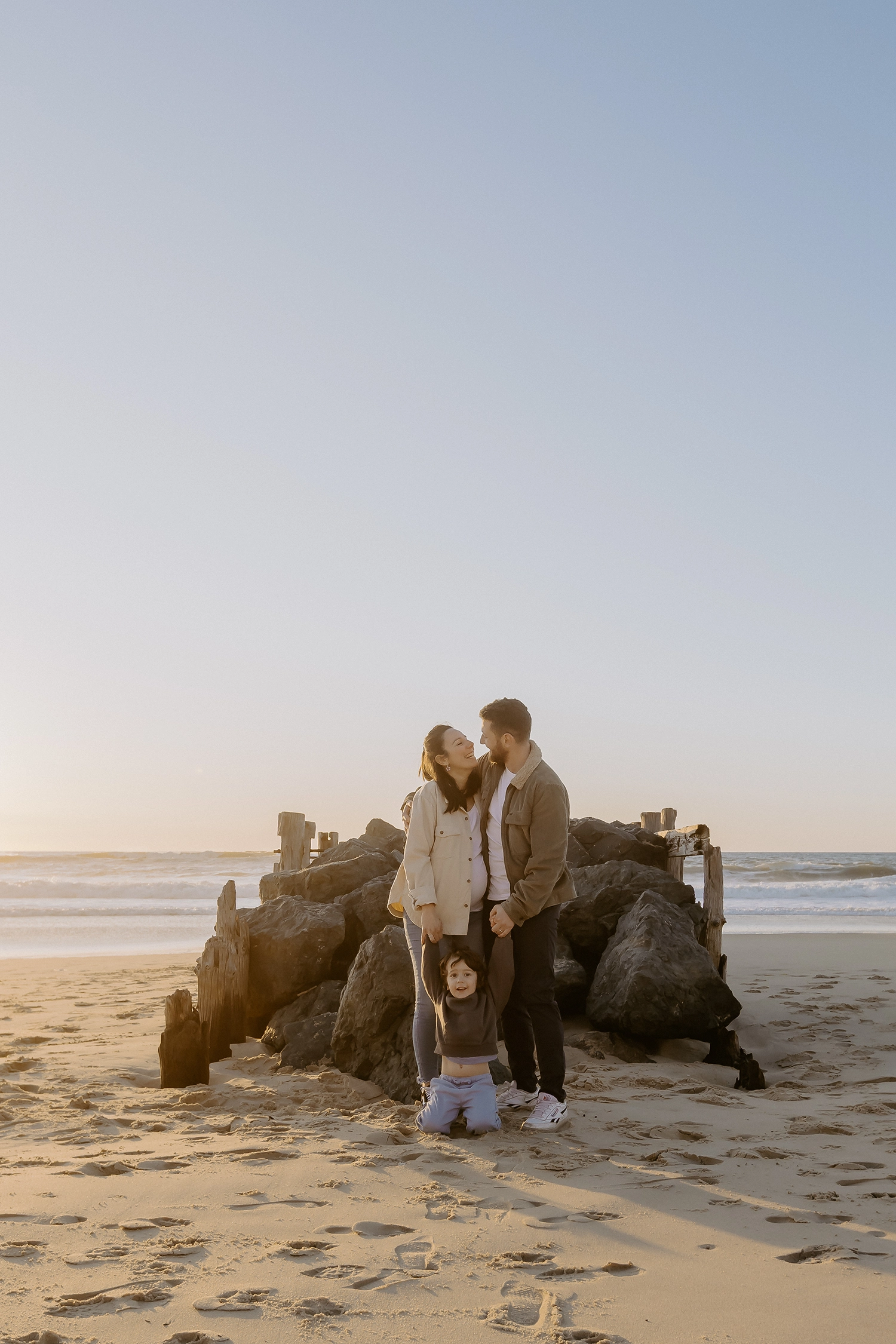 Couple souriant, main dans la main, attendant leur deuxième enfant sur le sable landais