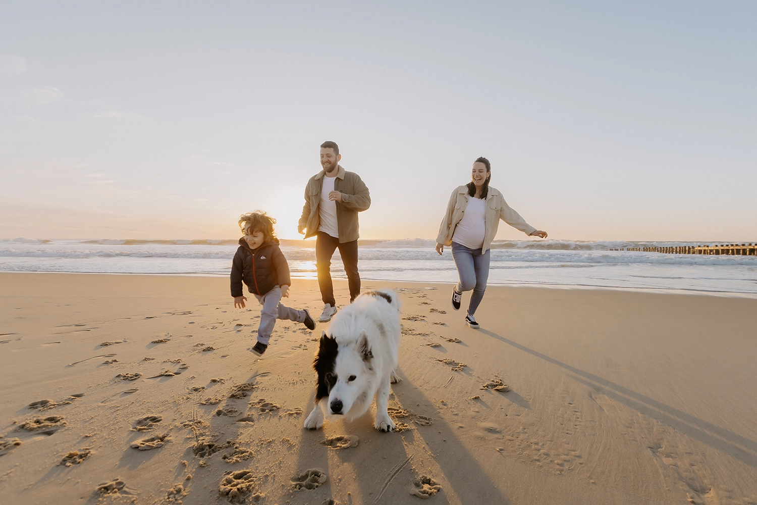Couple souriant, main dans la main, attendant leur deuxième enfant sur le sable landais