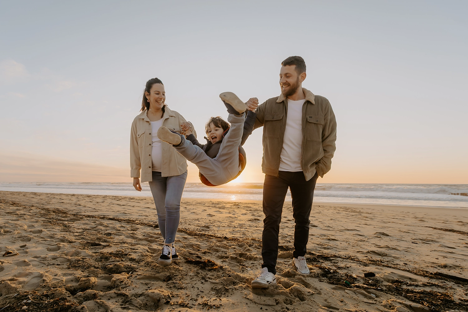 Couple souriant, main dans la main, attendant leur deuxième enfant sur le sable landais